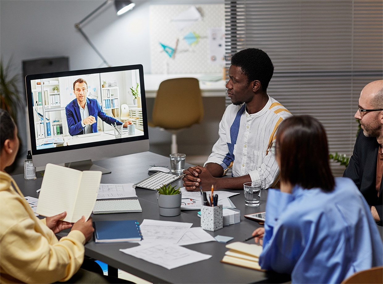 Team round a table looking at presenter on screen